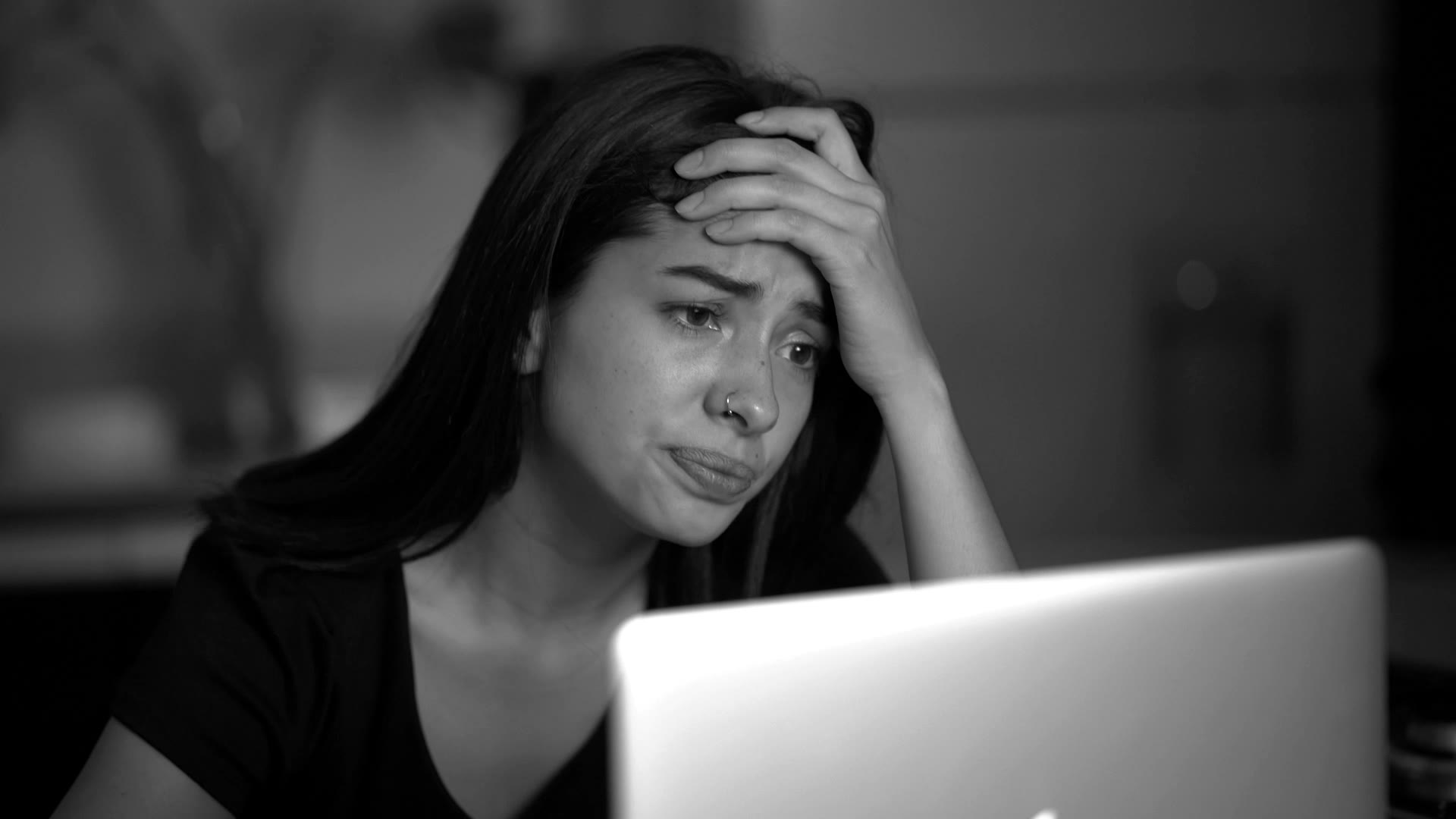 Een vrouw achter haar laptop, met haar hand op haar voorhoofd